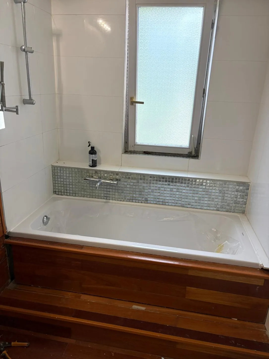 Baignoire neuve sous une fenêtre, frise mosaïque et habillage en bois