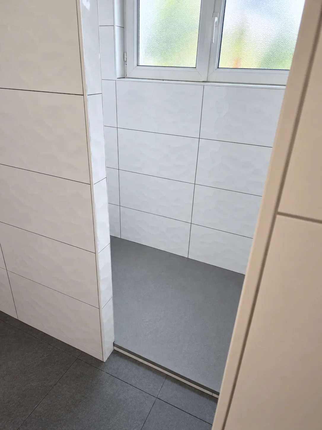 Douche en cours de travaux : faïence blanche posée sous une fenêtre, équipements pas encore installés
