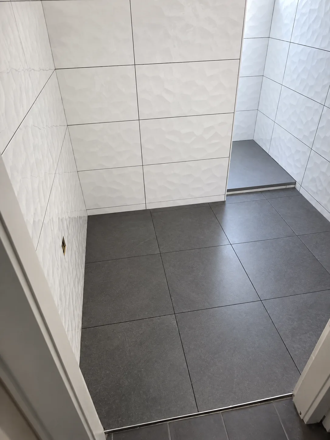 Salle de bain en cours de travaux : faïence blanche en relief et grand carrelage gris ardoise au sol
